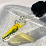 Golden 2% Bakuchiol Overnight Oil dripping from the dropper, showing the black seed facial oil texture