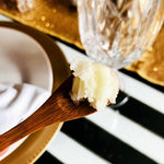 Makeup-Melting Cleansing Balm texture on a wooden spoon beside a glass