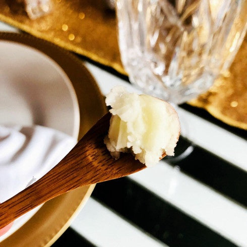 Makeup-Melting Cleansing Balm texture on a wooden spoon beside a glass