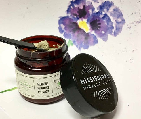 Open Morning Minerals Eye Mask jar with a spoon and pansy flowers, showing the mineral mask